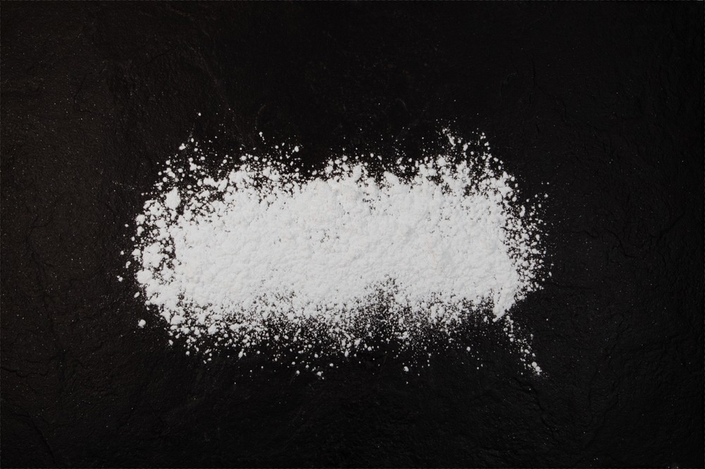 Silicon dioxide powder or Silica. Food additive E551, anti-caking agent. Silicon oxide. White chemical dust scattered on dark surface.