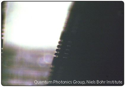 Optical microscope image from the LatticeAx shows the cleaved sample with the nanophotonic structures protruding from the edge of the chip. Courtesy of the Quantum Photonics Group, Niels Bohr Institute, University of Copenhagen.