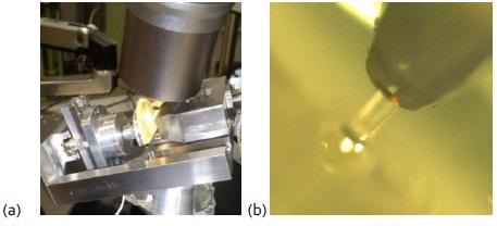 (a) Experimental set-up comprising of an Alemnis indenter used under a Keyence optical microscope for microcompression of polymer fibers, and (b) optical image of a fiber during compression with a flat punch.