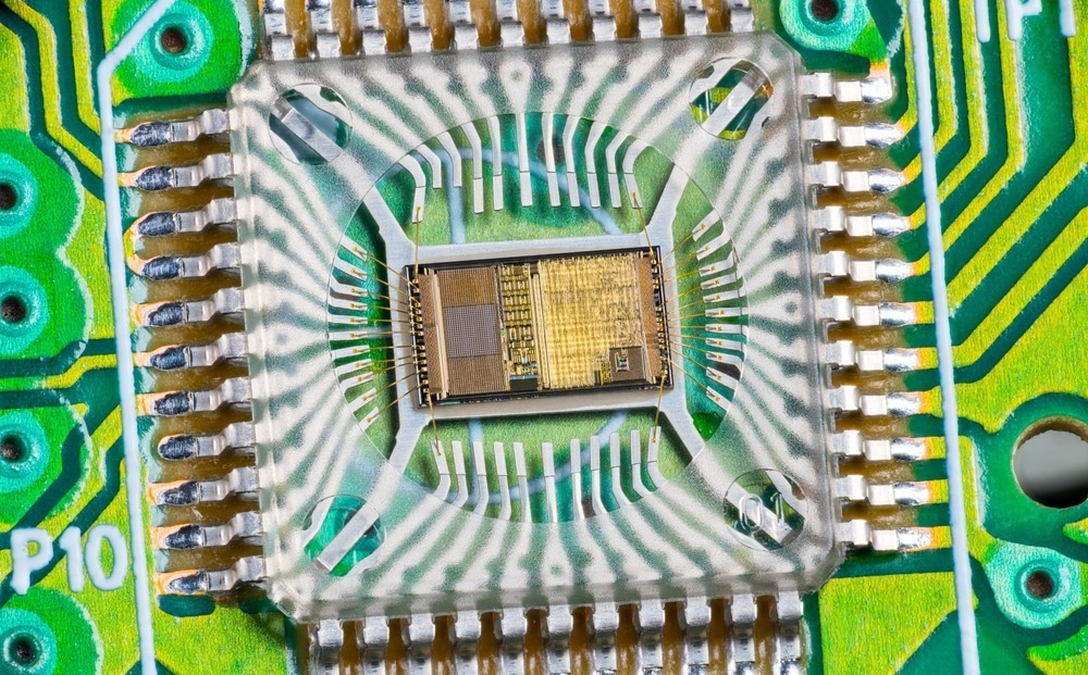 Closeup of electronic integrated circuit die with photodiode array and gold wires on green PCB. Micro chip inside optical computer mouse image sensor in plastic package with round hole and metal pins.